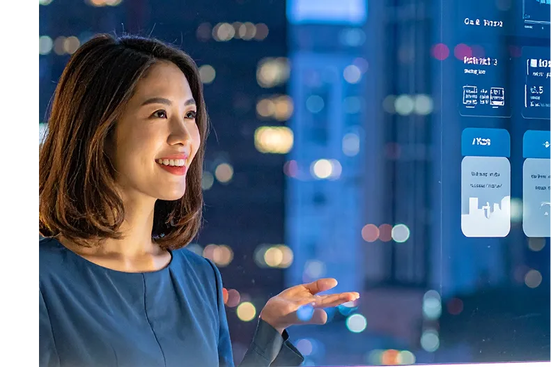 Smiling woman interacting with a transparent digital interface in a modern cityscape at night.